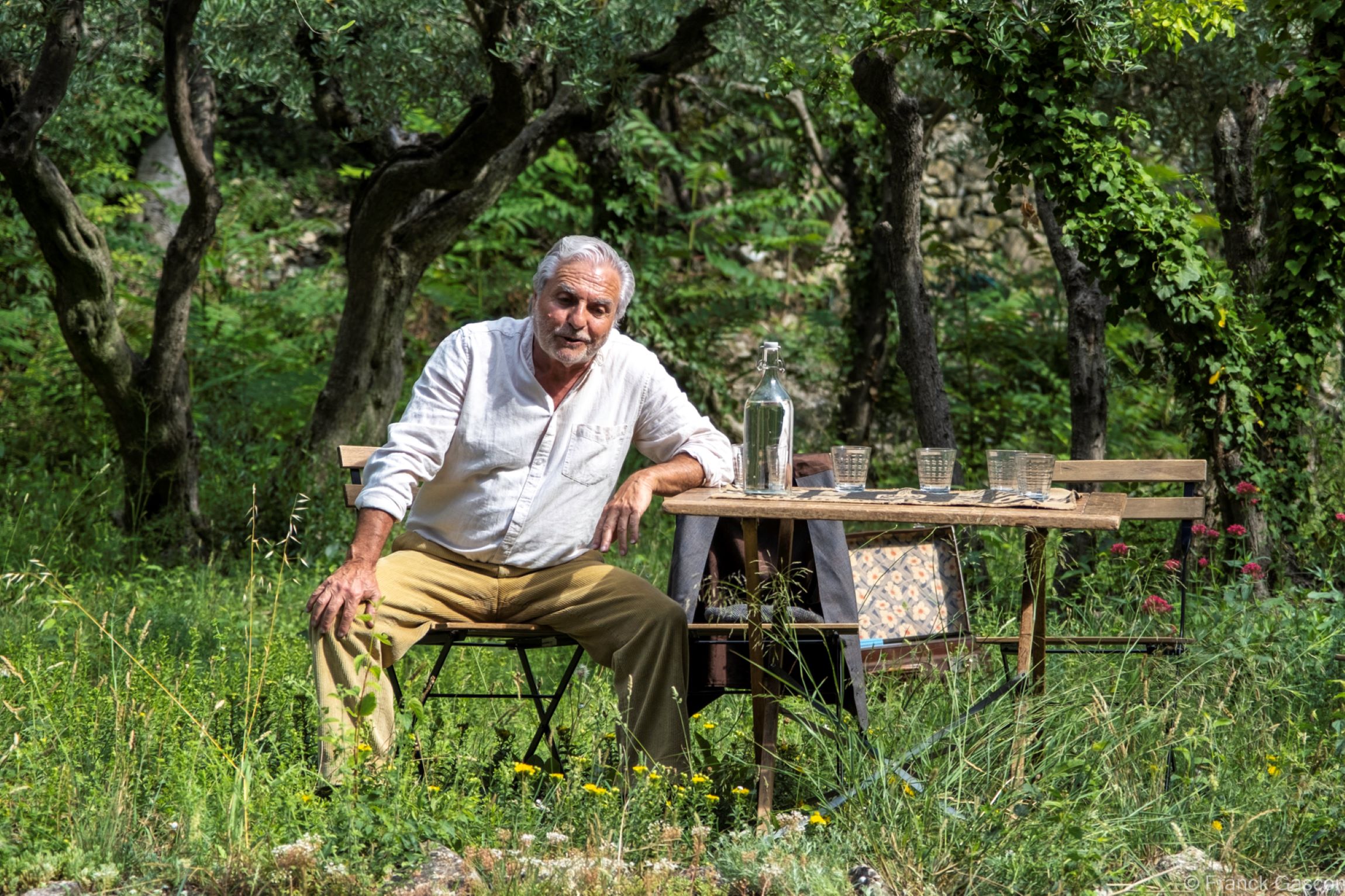 Photo du comedien accoudé a une table dans la nature spectacle Souvenirs des collines